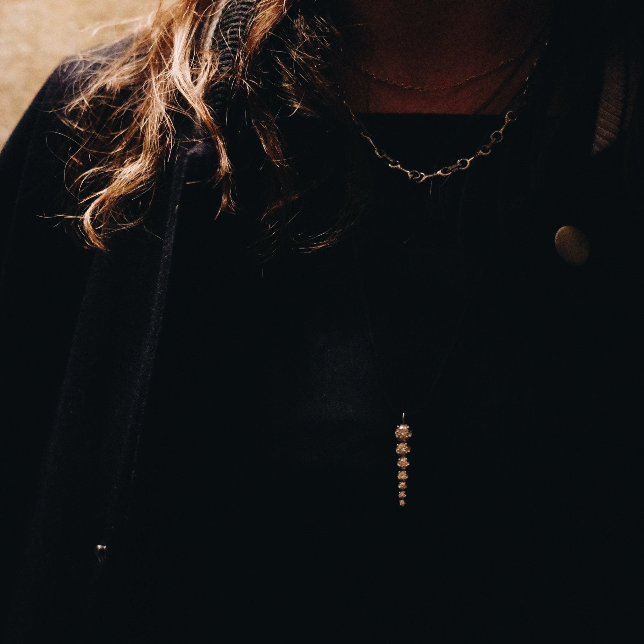Close-up of a person wearing a dark coat with a chain detail on a blurred background