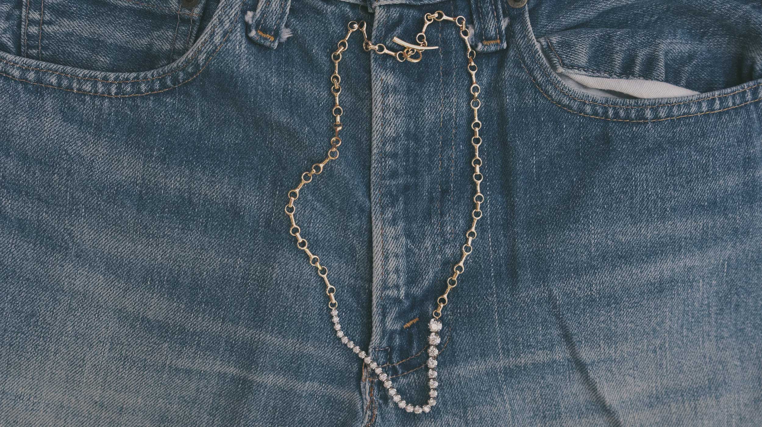 Close-up of a tennis chain necklace draped over blue jeans.