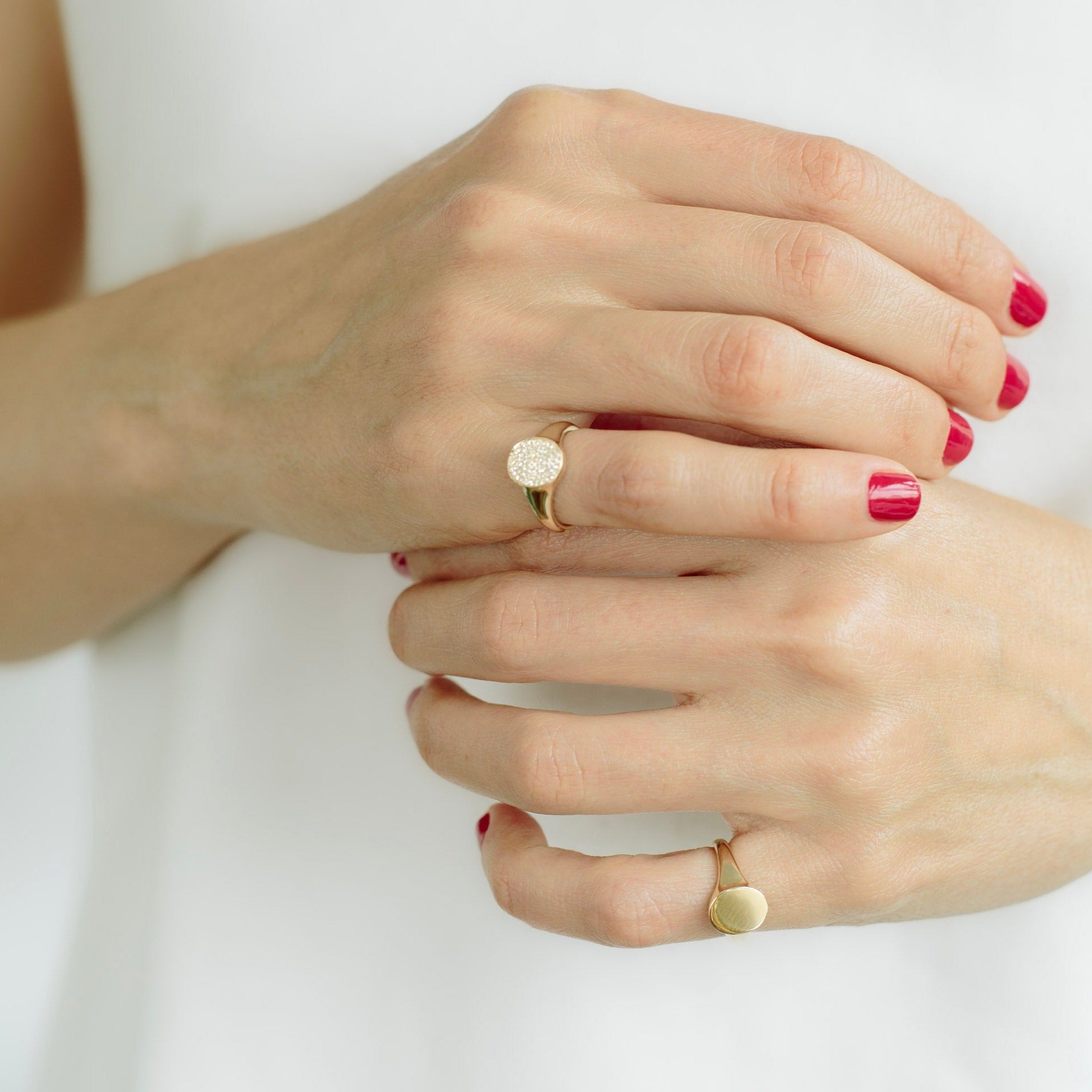 A close-up of a girl's finger showcasing a disc signet ring embellished with white pavé diamonds - Gabriela Artigas