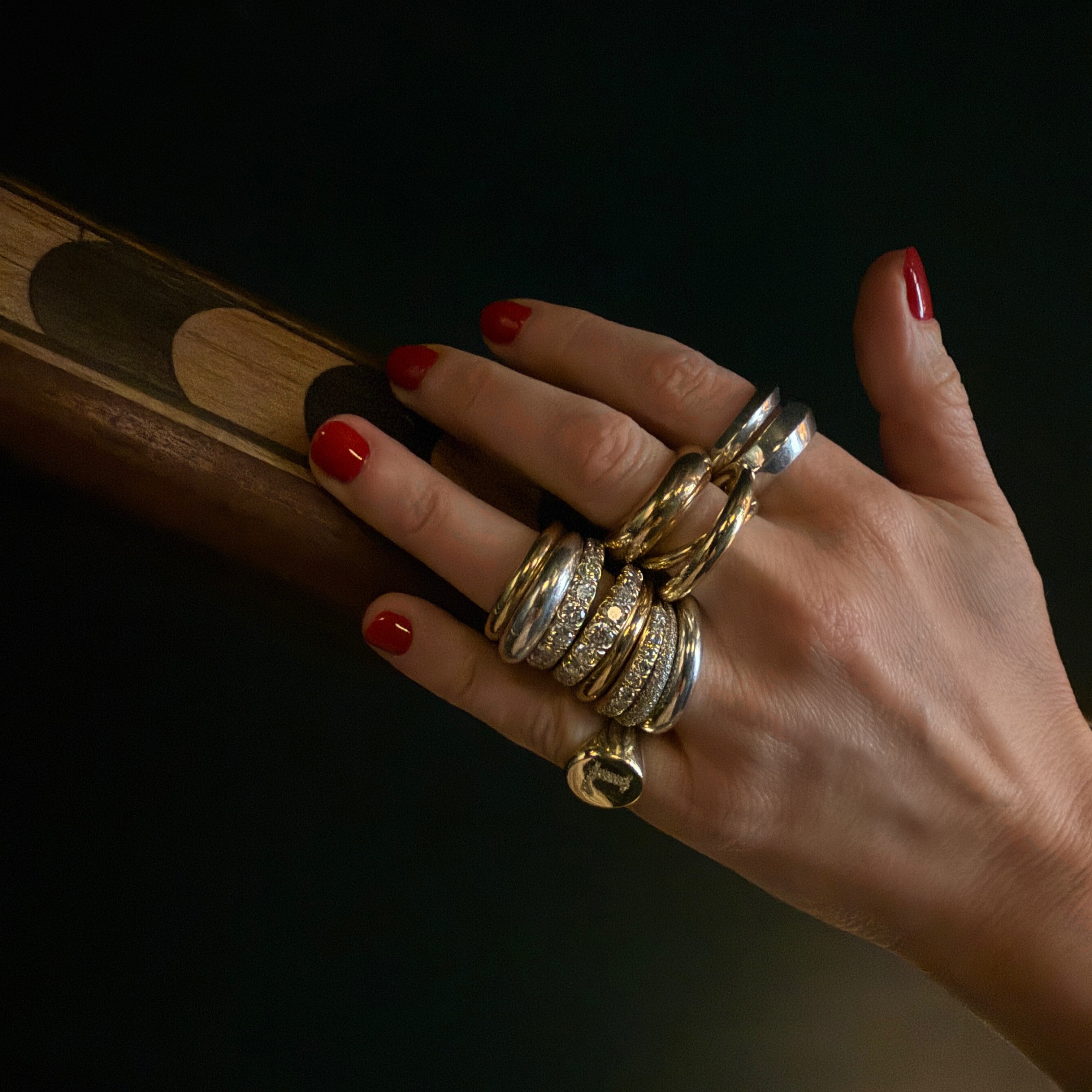 Hand wearing multiple gold and diamond rings on a dark backgrounnd from Gabriela Artigas & Co