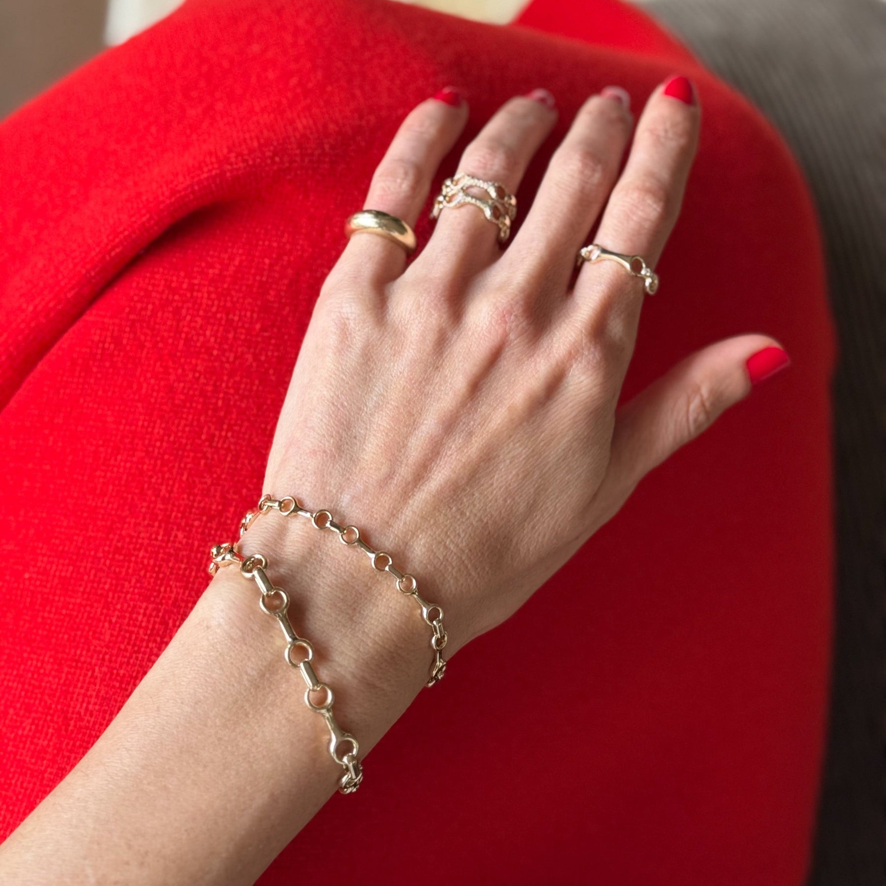 Hand with gold rings and bracelet on a red surface